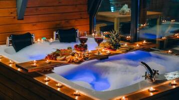 A hot tub with candles, fruits, and glasses of red wine.