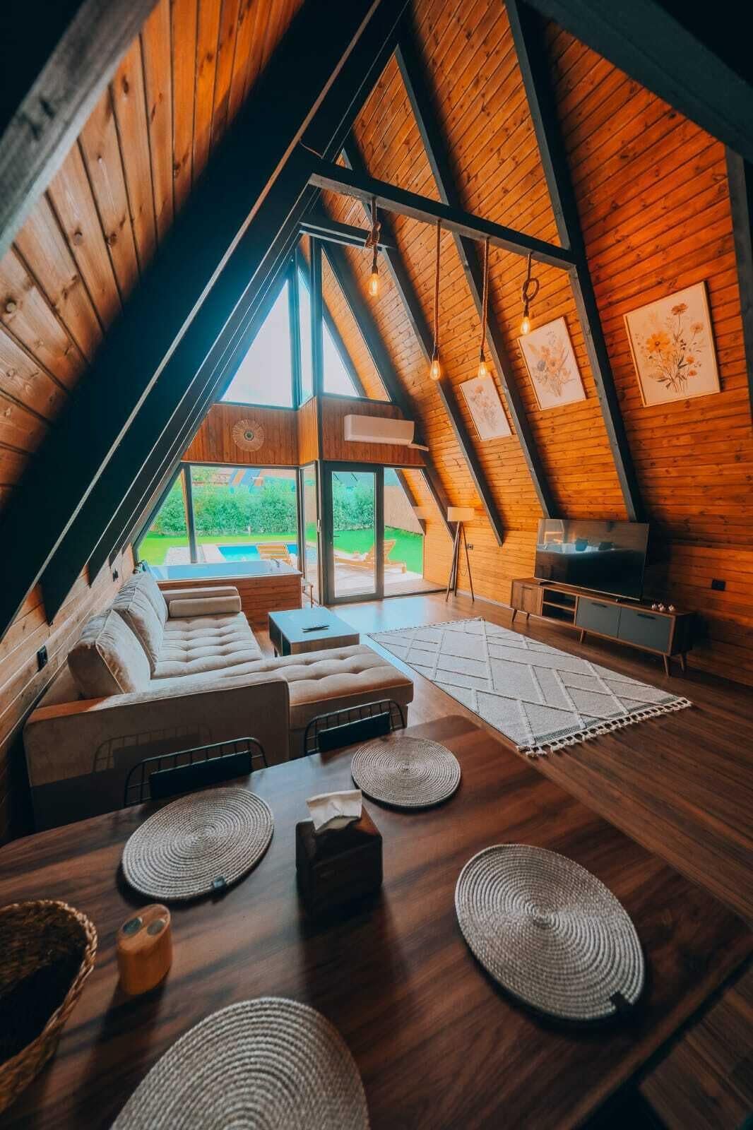 An attic room with a wooden sloped ceiling, a sofa set, a dining table, and a TV.