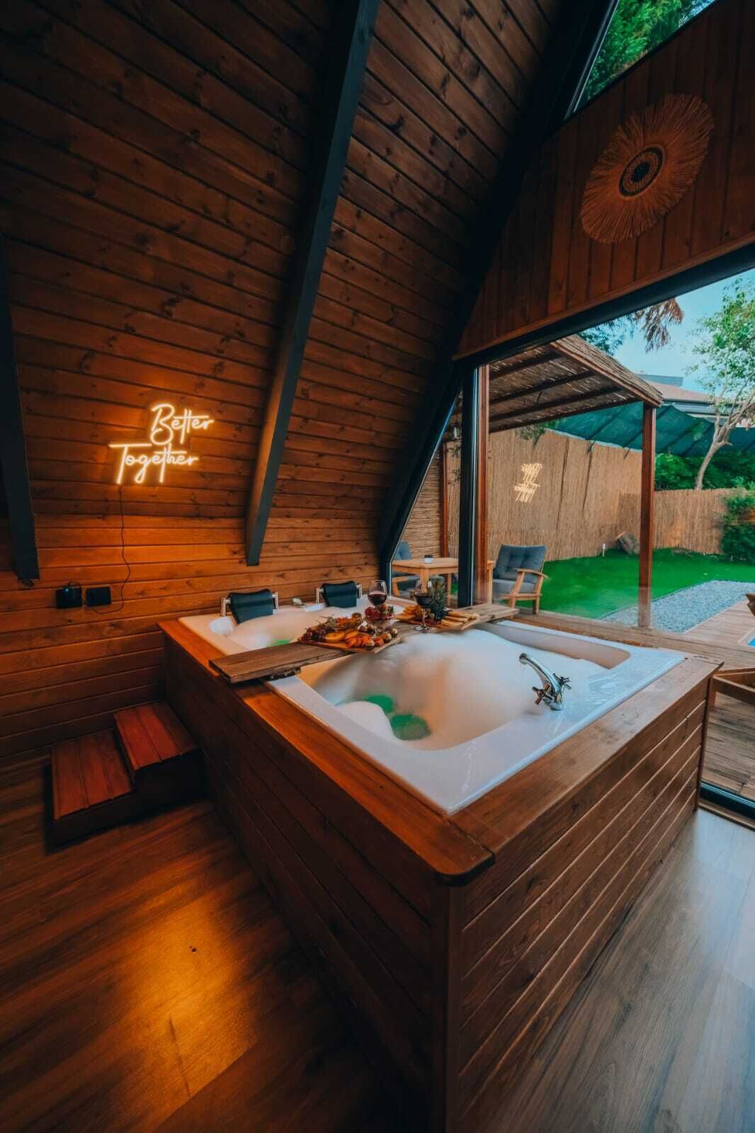 A wooden cabin interior with a large bathtub, a neon sign, and a view of the outdoors.