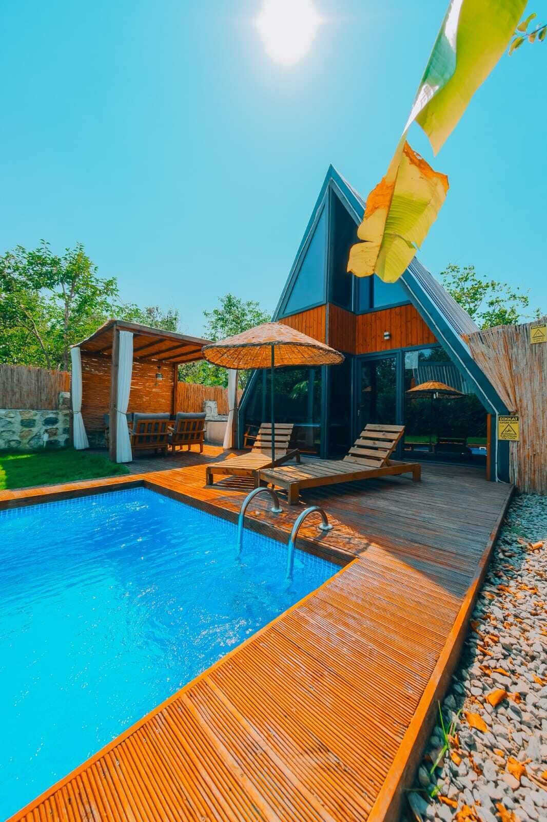 A modern outdoor pool area with a wooden deck, lounge chairs, and umbrellas.