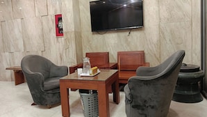 A hotel room with a flat-screen TV mounted on the wall, a wooden table with two chairs, and a small trash bin. - Kingston Home (Nha Trang)