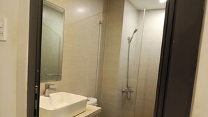 A bathroom with a white sink, a toilet, and a glass-enclosed shower area. - Kingston Home (Nha Trang)