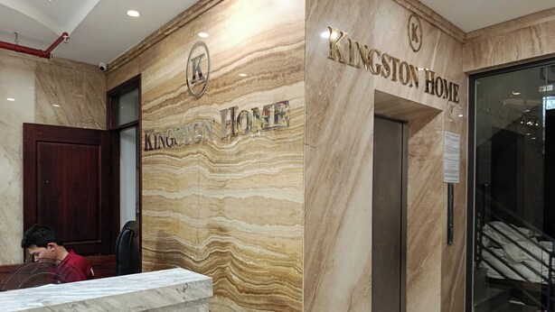 A reception area with a marble wall, a wooden door, and a sign that reads 'KINGSTON HOME'. - Kingston Home (Nha Trang)