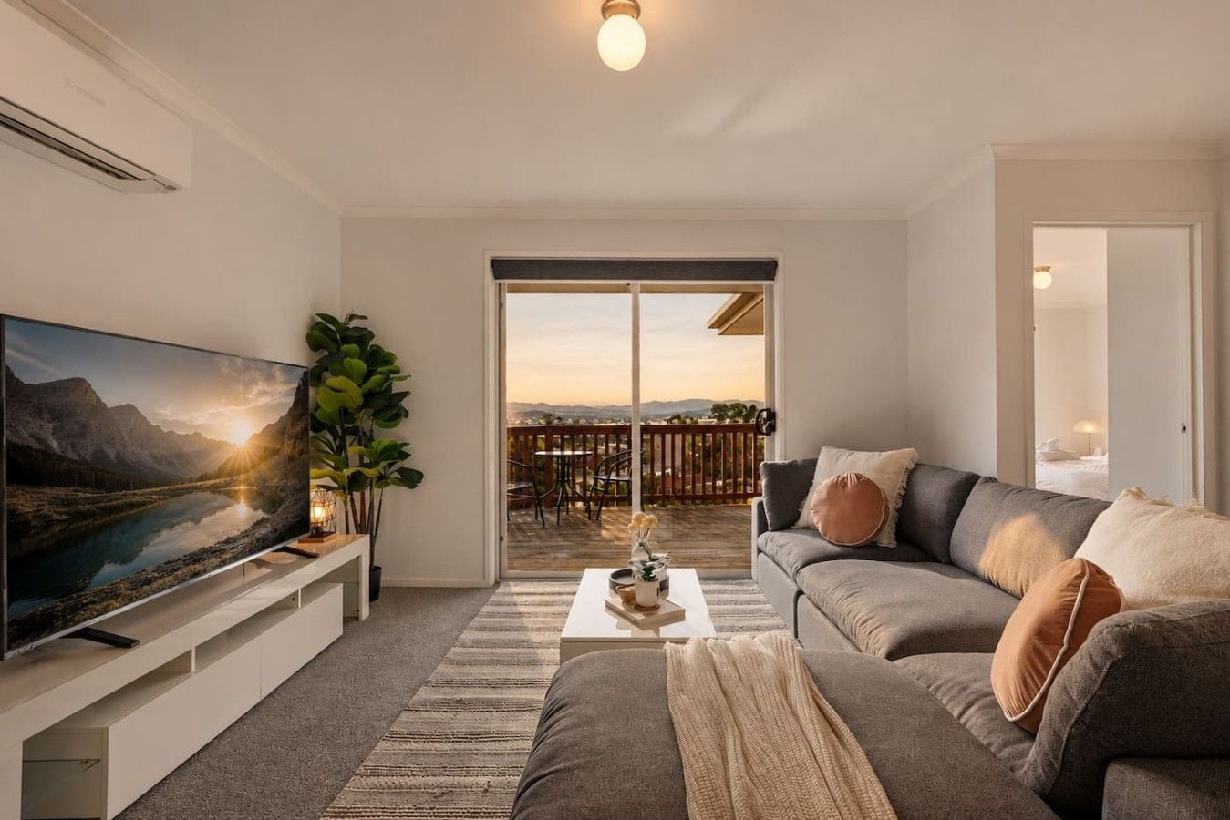 Una sala de estar moderna con un televisor de pantalla plana, un sofá gris, una mesa de centro y un ventanal con vistas a una terraza.