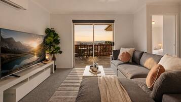 Una sala de estar moderna con un televisor de pantalla plana, un sofá gris, una mesa de centro y un ventanal con vistas a una terraza.