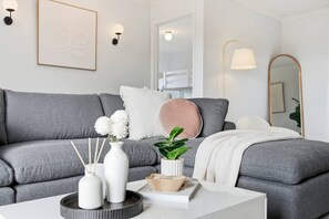 A modern living room with a grey sofa, white decorative items, and a mirror. - Mountain View Retreat | BBQ, Balcony & Parking (Glenorchy)