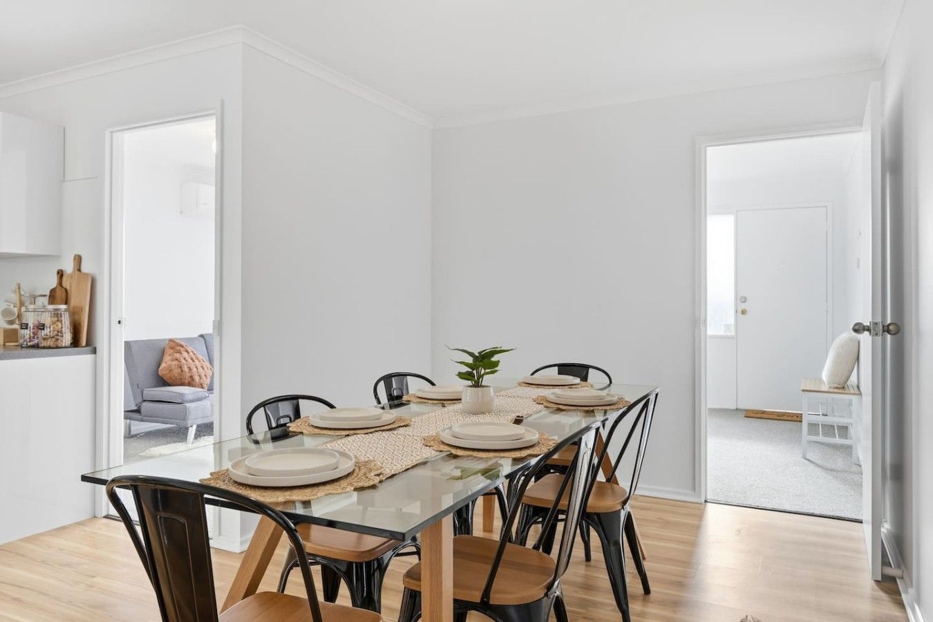 Moderni ruokailutila, jossa on lasipöytä, kuusi tuolia ja koristeellinen kasvi pöydän keskellä.
