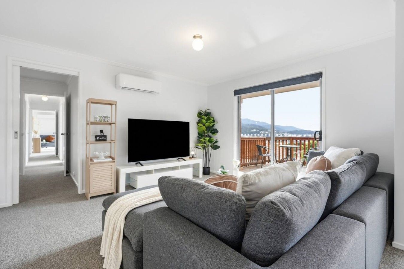 A modern living room with a grey sofa, a flat-screen TV, and a balcony with a view.