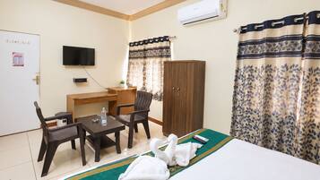 Habitación de hotel con cama, escritorio, dos sillas, televisor, aire acondicionado y cortinas.