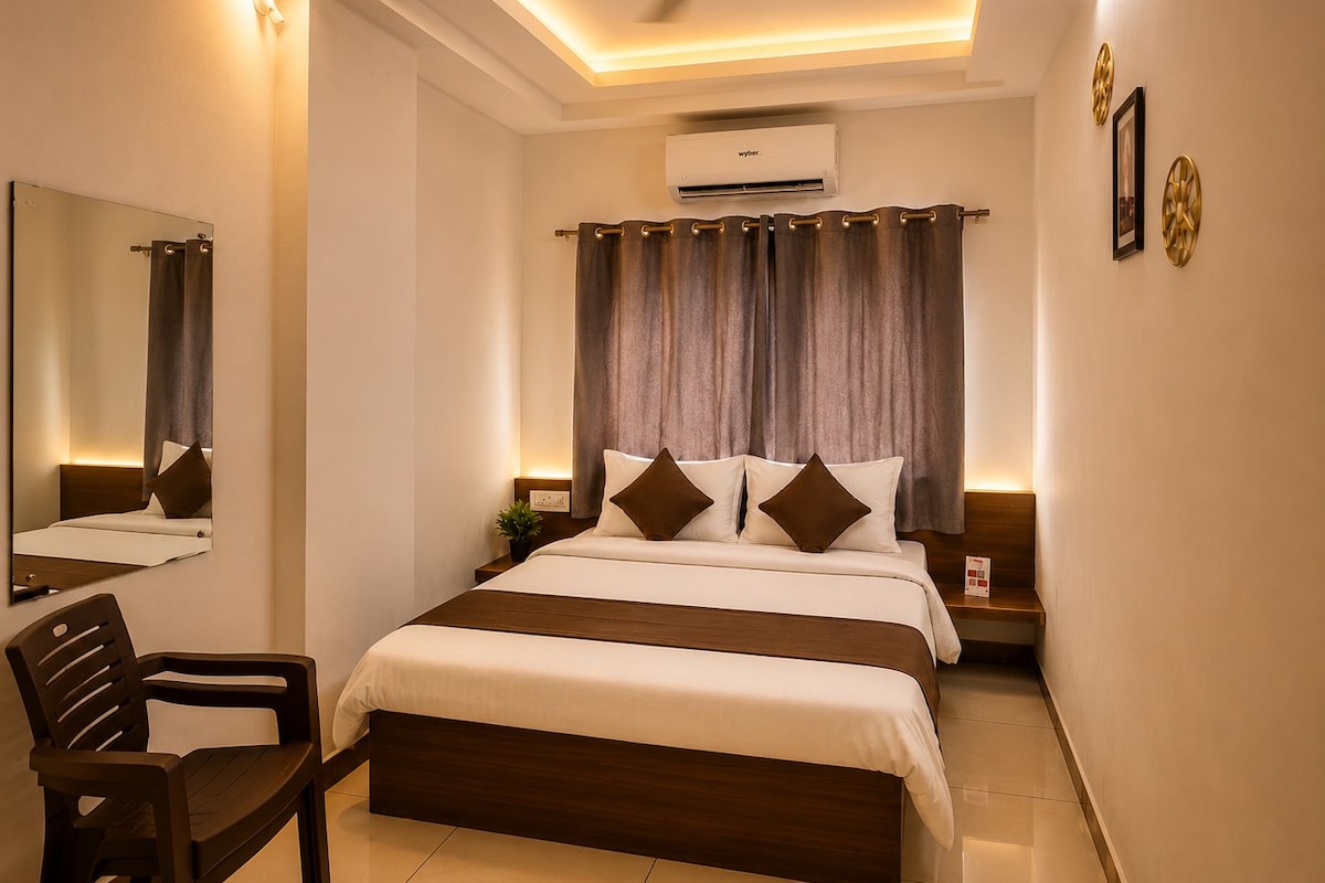 A hotel room with a bed, a chair, a ceiling fan, an air conditioning unit, and a wall-mounted mirror.