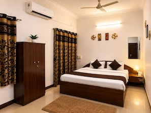 A hotel room with a bed, a wardrobe, a ceiling fan, an air conditioning unit, and a small bedside table with a lamp. - Hotel The One (Rajkot)