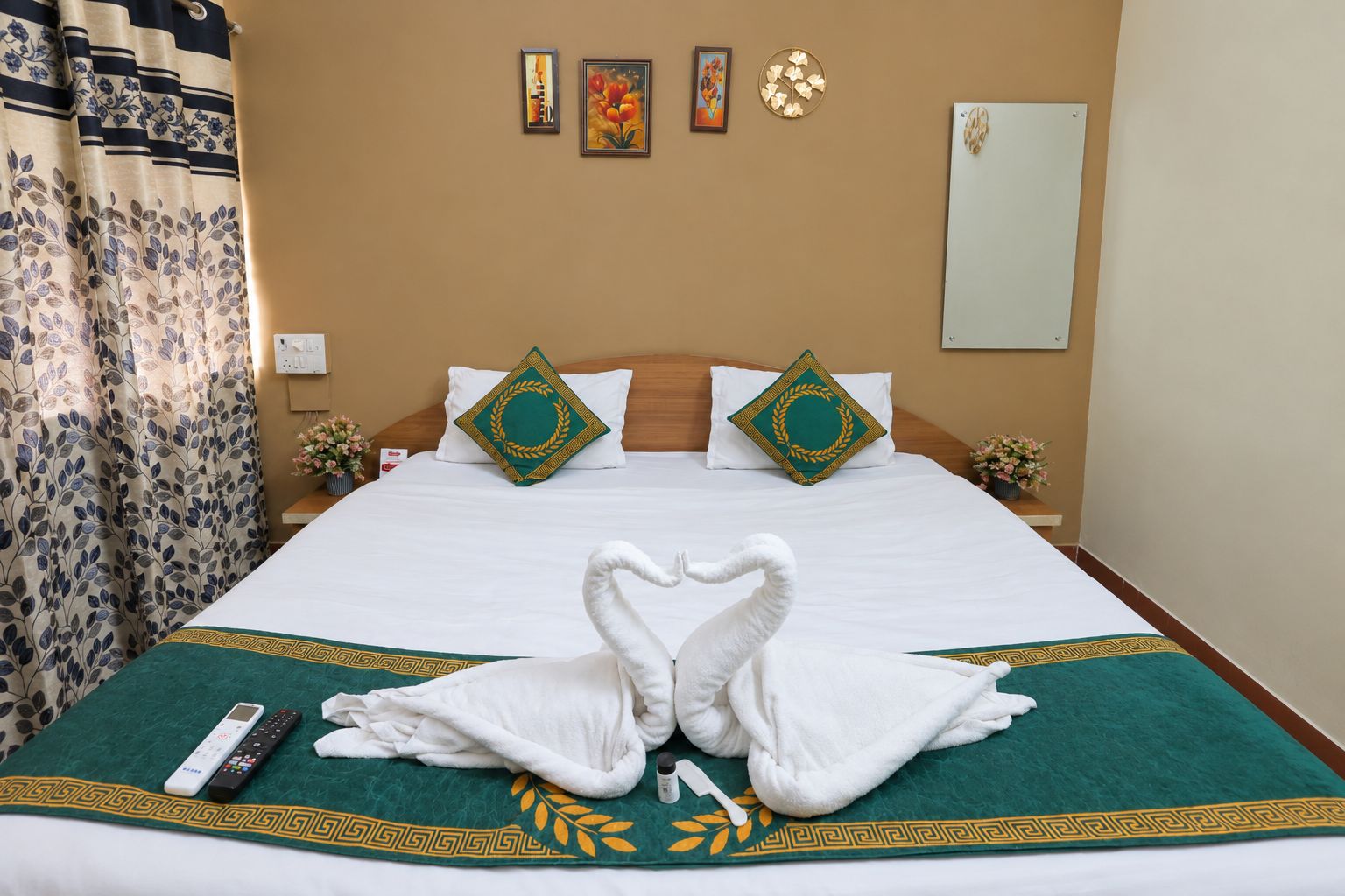 A hotel room with a bed, pillows, a remote control, and a decorative towel arrangement.