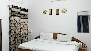 A bedroom with a bed, a curtain, a wall-mounted mirror, and three framed pictures. - Hotel The One (Rajkot)