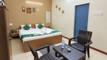 Quarto de hotel com cama, duas cadeiras, mesa, mesinha de cabeceira, relógio de parede, espelho, porta e parede decorada com pratos.