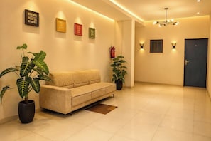 A modern living room with a beige sofa, two potted plants, and motivational wall art. - Hotel The One (Rajkot)