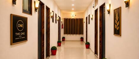 A hotel corridor with framed artwork, wall-mounted lights, and potted plants.