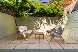 A patio with two wooden chairs and a small table, surrounded by a white fence and lush greenery. - Sunlit Sands End Terrace & Garden (London)