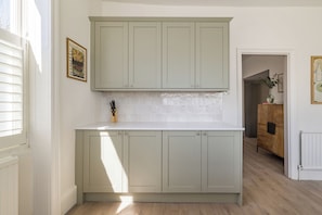 A kitchen with light-colored cabinets, a white countertop, and a backsplash. - Sunlit Sands End Terrace & Garden (London)