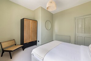 A bedroom with a bed, a wardrobe, a chair, and a wall-mounted circular light fixture. - Sunlit Sands End Terrace & Garden (London)