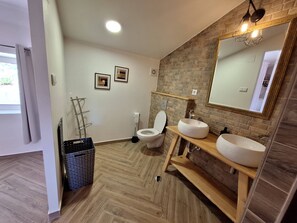Een moderne badkamer met een visgraatvloer, een toilet, een wastafel en een spiegel met verlichting.