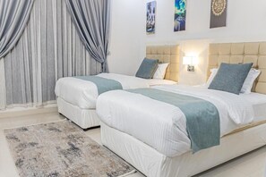 Habitació d'hotel amb dos llits, una finestra gran amb cortines, una taula de nit amb una làmpada i una obra d'art a la paret.