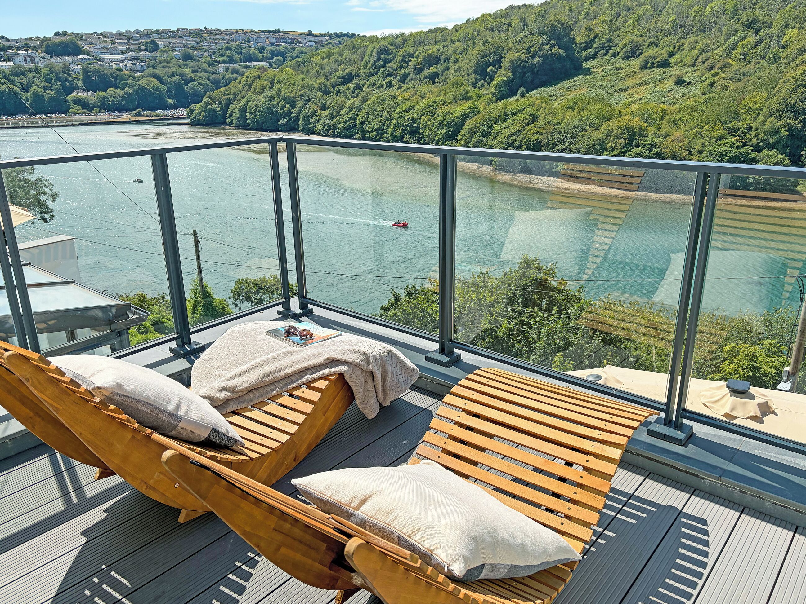 Un balcón con sillones de madera y barandilla de cristal con vistas al río.