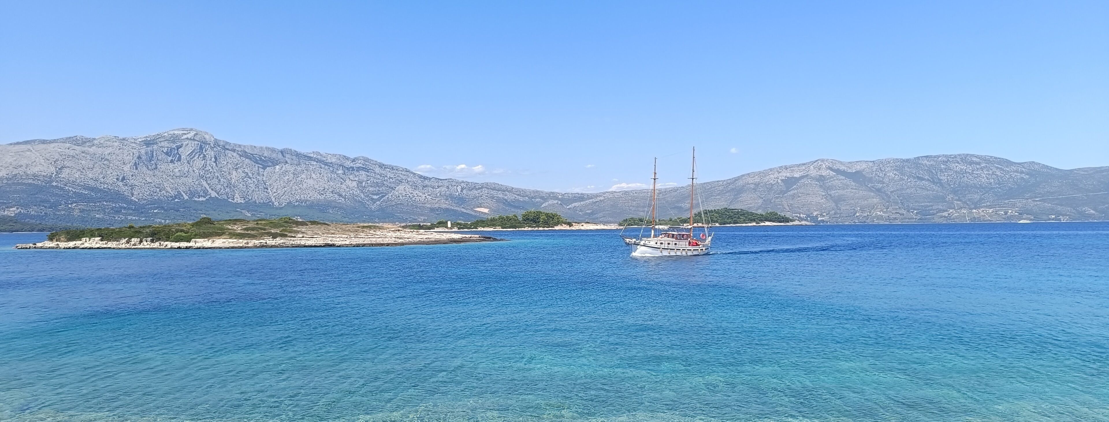 A boat on a clear blue sea with mountains in the background.
