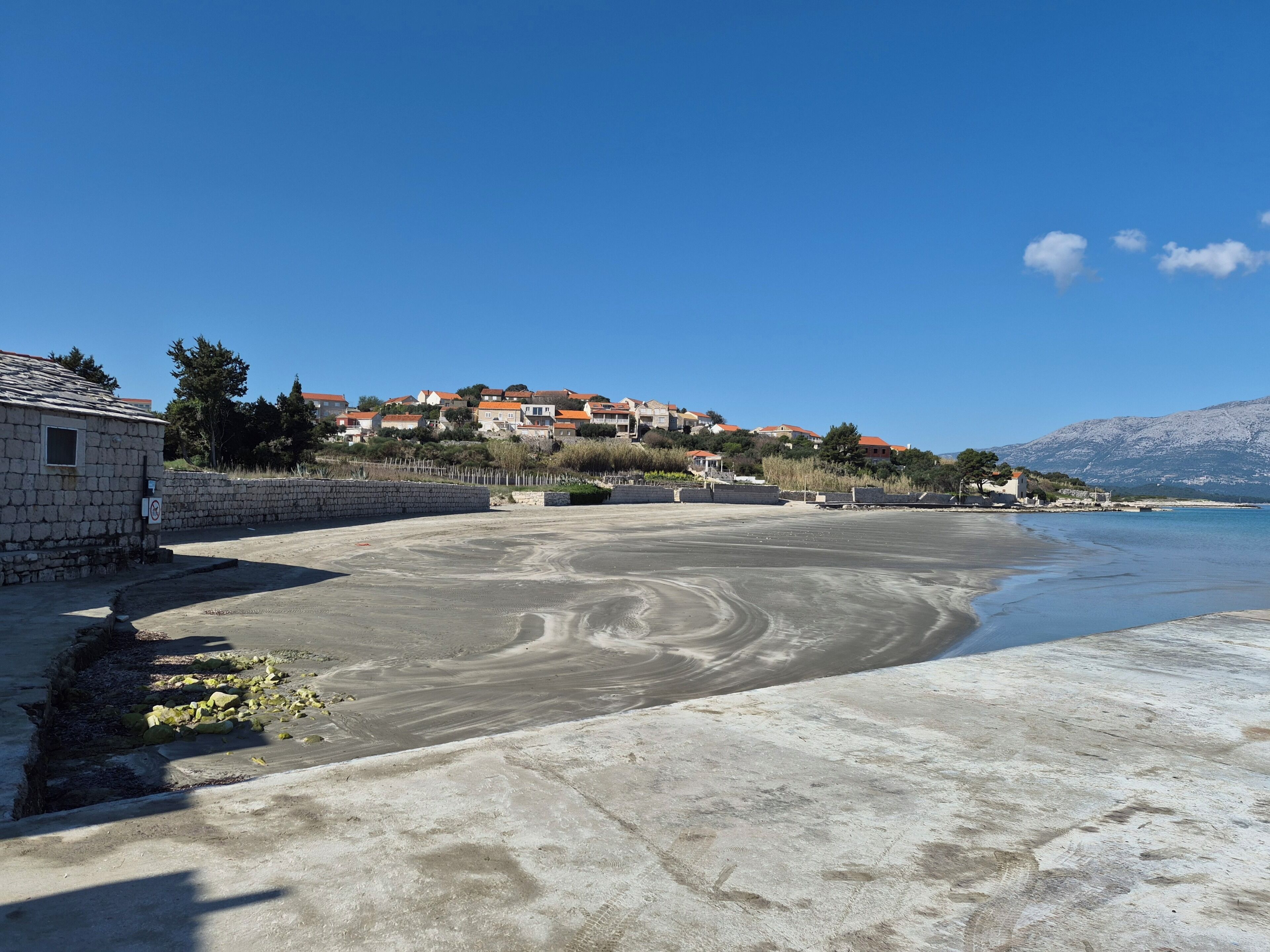 Une zone côtière avec une plage de sable, un mur de pierres et une rangée de maisons aux toits rouges.