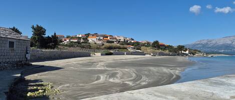 Une zone côtière avec une plage de sable, un mur de pierres et une rangée de maisons aux toits rouges.