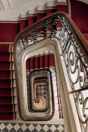 A spiral staircase with red carpeted steps and ornate black metal railings. - Luxurious Suite A/C - 2P - Madeleine/saint-honore (Paris)
