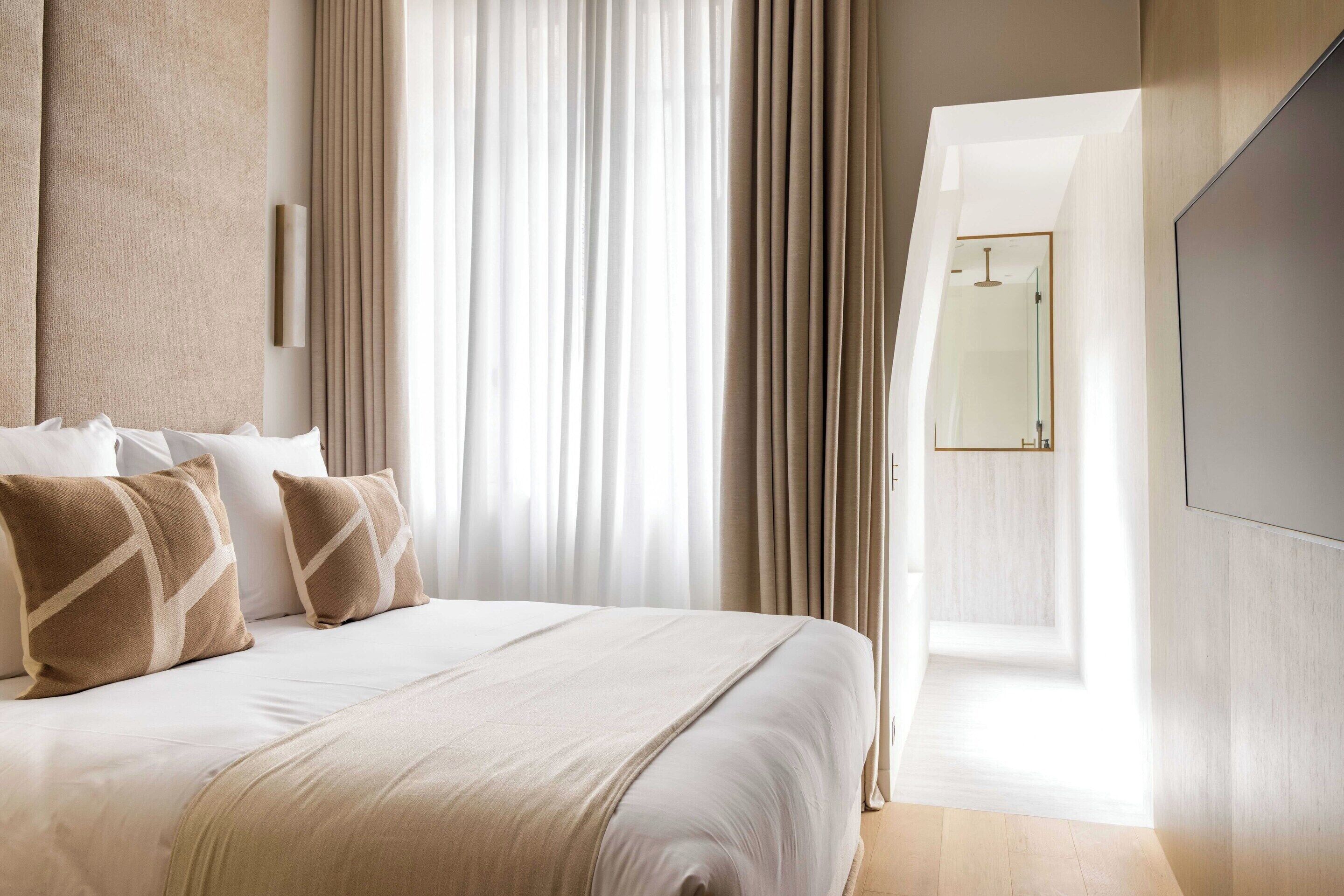 A modern hotel room with a large bed, a flat-screen TV, and a view of the city through the window.