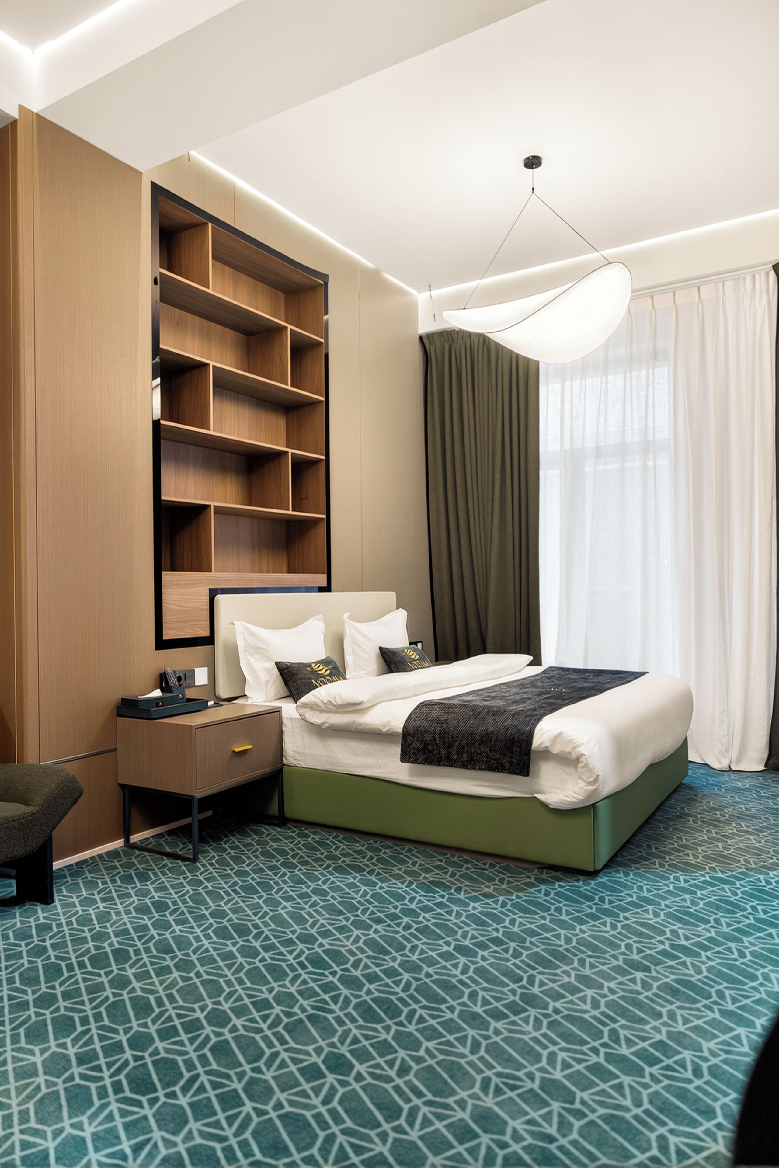 A hotel room with a bed, a desk, a chair, a wardrobe, and a large window with curtains.
