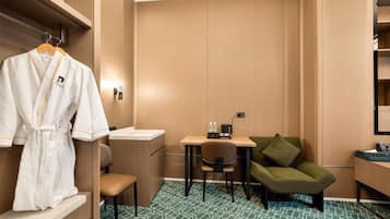 A hotel room with a wooden wardrobe, a desk with a chair, a small sofa, and a robe hanging on a rack.