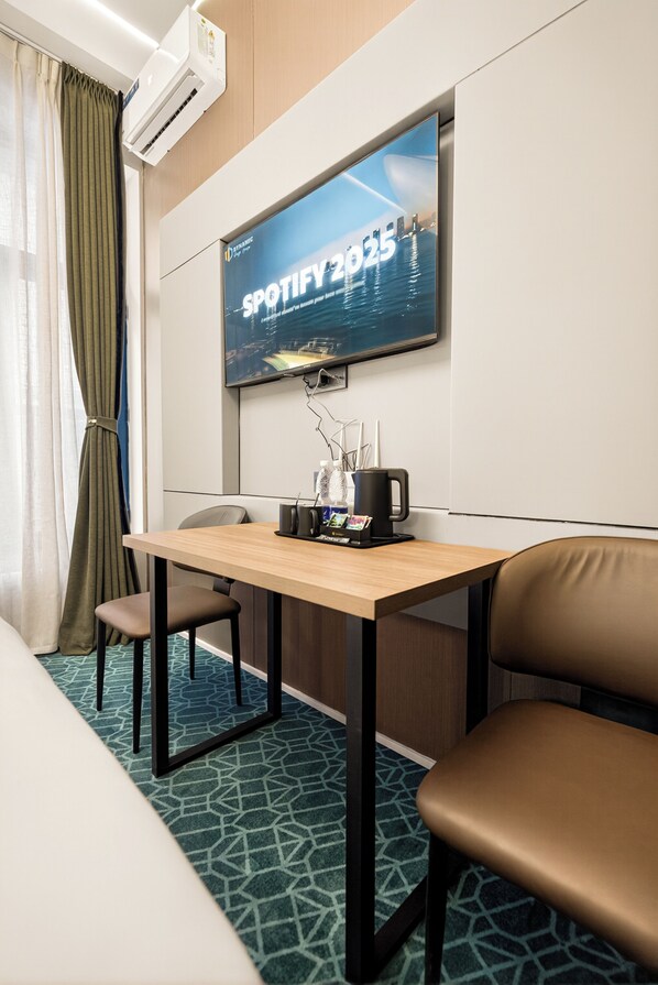 Habitación de hotel con cama, una mesa y sillas, televisión en la pared y aire acondicionado.