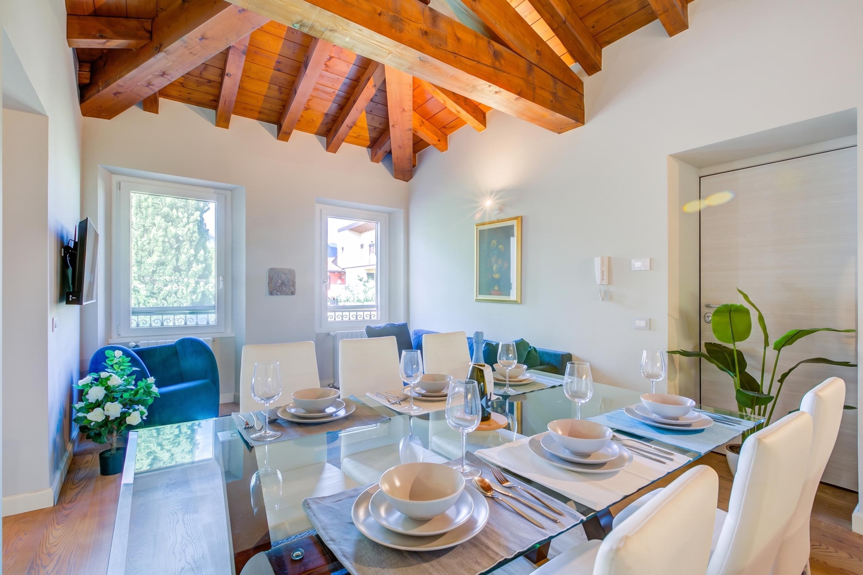 A dining area with a glass table set for six, white chairs, and a wooden ceiling.