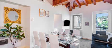 Un comedor con una mesa de vidrio y sillas blancas, una planta en maceta y un espejo grande en la pared.