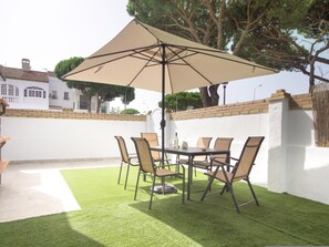 An outdoor patio with a table and chairs, a large umbrella, and a brick wall. - las Torres 215 in Chiclana de la Frontera (Chiclana de la Frontera)