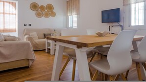 A modern living room with a wooden dining table, white chairs, a sofa, and a television. - las Torres 215 in Chiclana de la Frontera (Chiclana de la Frontera)