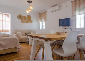 Ein modernes Wohnzimmer mit einem Holzesstisch, weißen Stühlen, einer Couch und einem Fernseher.