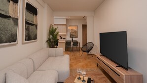 Ett modernt vardagsrum med en hörnsoffa, en platt-TV på ett träställ och en matplats i bakgrunden.
