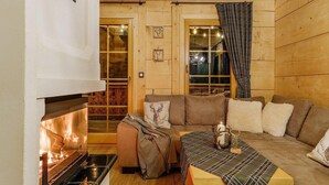 Ein gemütliches Blockhauss-Interieur mit Kamin, einer Couch, einem Tisch und einem Fenster mit Vorhängen.