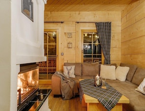 A cozy cabin interior with a fireplace, a sofa, a table, and a window with curtains. - Stylish Highlander Holiday Home, Sauna, Jacuzzi (Poronin)