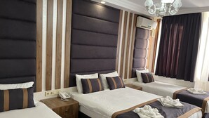 A hotel room with a large bed, two smaller beds, a bedside table with a phone, and a chandelier. - New Room Hotel (İstanbul)
