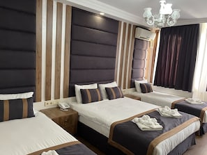 A hotel room with a large bed, two smaller beds, a bedside table with a phone, and a chandelier. - New Room Hotel (İstanbul)