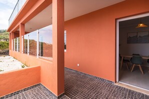 A modern building with a balcony, a dining area with chairs and a table, and a view of the surrounding landscape. - GuestReady - Casa da Vereda (Arco da Calheta)