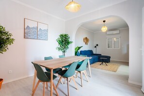 A modern living space with a dining area, a sofa, and a large window. - GuestReady - Casa da Vereda (Arco da Calheta)