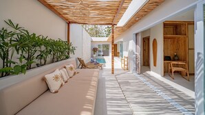 A sunlit outdoor seating area with a sofa, cushions, and potted plants. - Rocha Villa Uluwatu (Uluwatu)