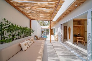 A sunlit outdoor seating area with a sofa, cushions, and potted plants. - Rocha Villa Uluwatu (Uluwatu)