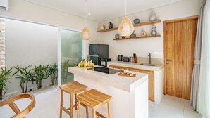 A modern kitchen with a central island, wooden stools, and a glass door leading to a balcony. - Rocha Villa Uluwatu (Uluwatu)