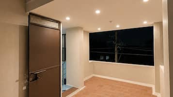 Un balcón con piso de baldosas, una puerta cerrada con reja metálica y vista al cielo nocturno.